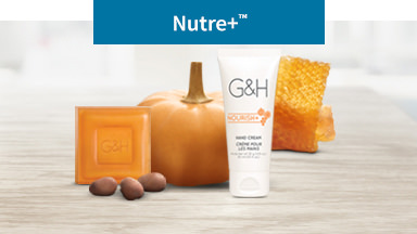 La imagen de fondo muestra la crema para Manos, Jabón de barra para la piel G&H rodeada de una calabaza, un panal de abejas y nueces karité. Los productos Amway para hidratar tu piel.