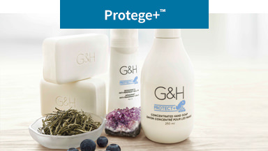 La imagen de fondo muestra el Jabón para Manos, Barra de Jabón y Desodorante y Antitranspirante Roll-On G&H rodeados de hojas secas de té blanco, arándanos y un cristal de amatista. Limpian y protegen tu piel.