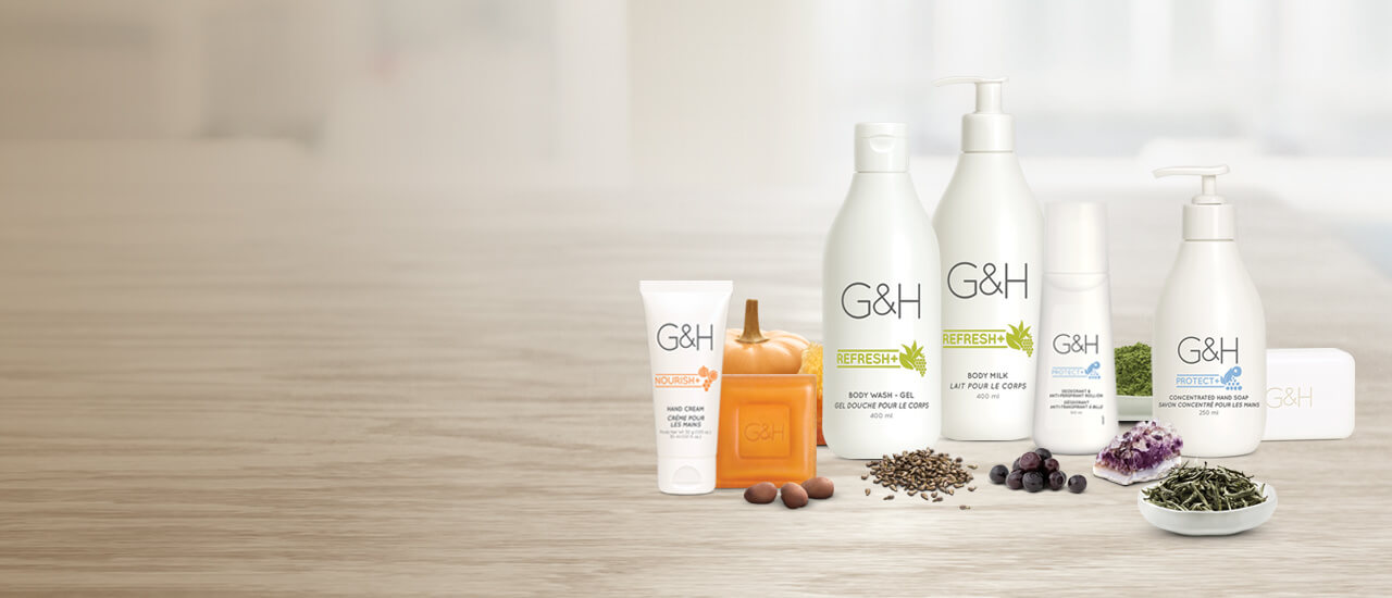 Productos G&H para el cuidado corporal rodeando los productos hay nueces, una calabaza pequeña, semillas de uva, arándanos, polvo de té verde, un cristal de amatista y hojas secas de té blanco. Ingredientes inspirados en la naturaleza.